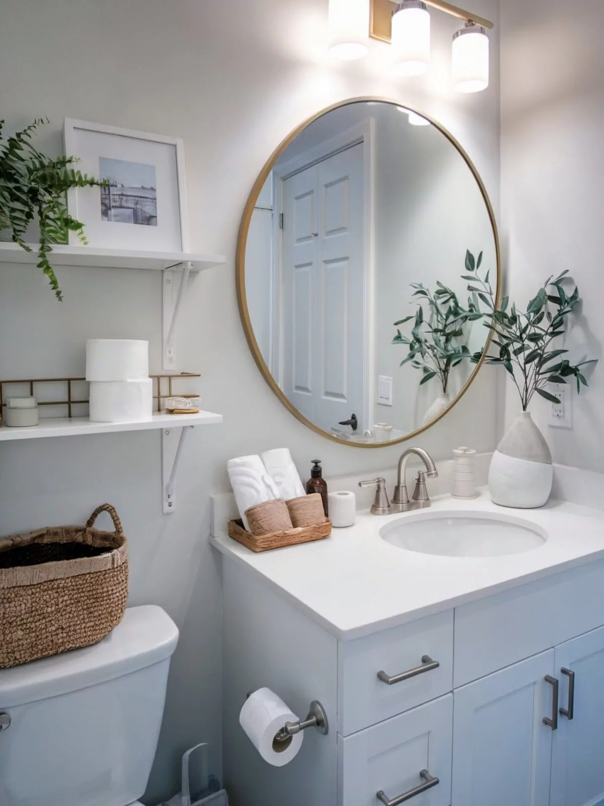 farmhouse bathroom vanity tray decor with gold rimmed round mirror above it and three cylindrical lights