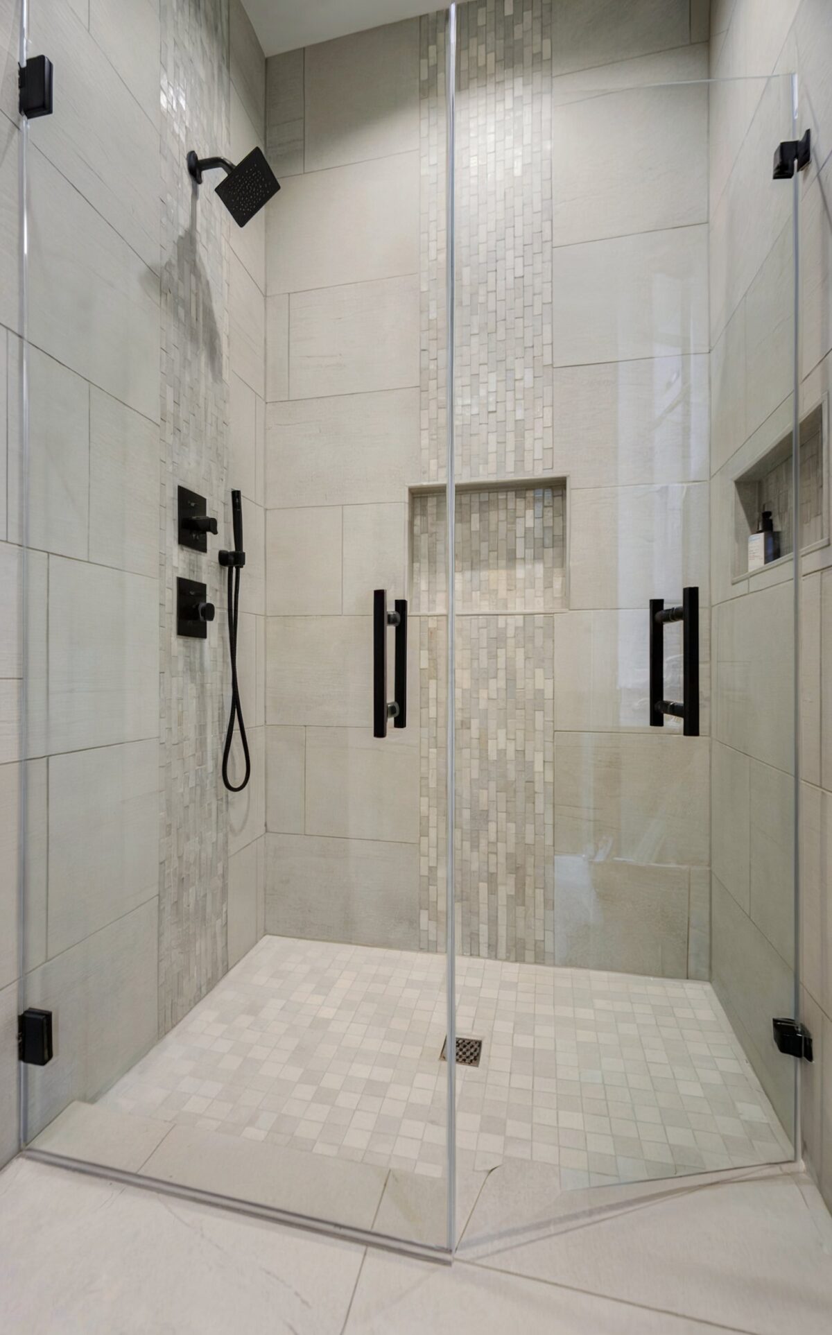 modern luxury bathroom small tile adorned with large, light gray tiles, a vertical accent of smaller, mosaic style tiles in a lighter shade
